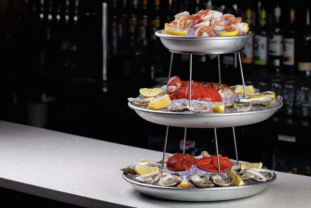 Three-tier seafood tower with oysters on the half shell, lobster claws, and shrimp cocktail on ice at PJ Lobster House in Port Jefferson, NY
